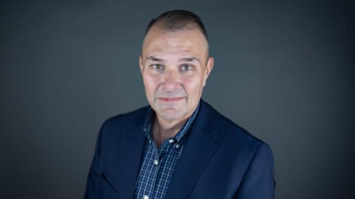 Dr. Rank wears a plaid button-up shirt and dark suit jacket for his headshot photo.